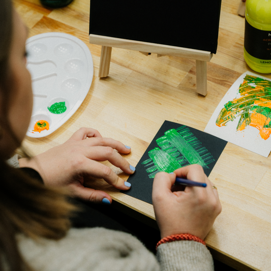 Eine Frau malt mit grüner Acrylfarbe ein Muster auf schwarzes Tonpapier in einem Workshop.