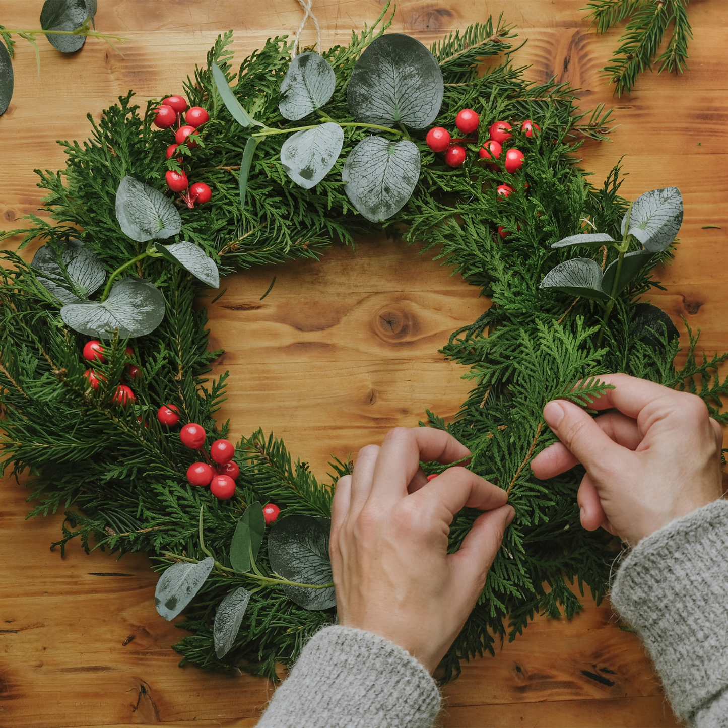 Zwei Hände binden mit Tannengrün einen Adventskranz im Workshop.