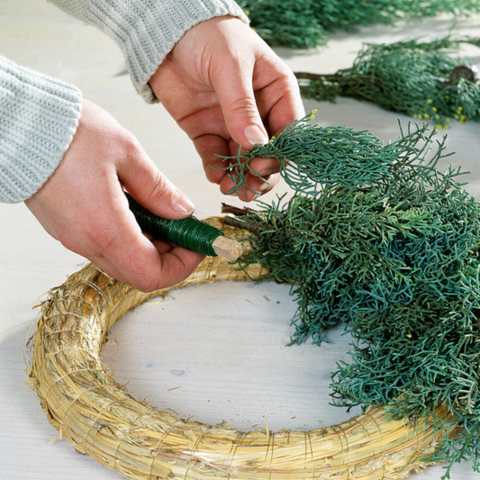 Zwei Hände binden einen Adventskranz im Kreativstudio München.