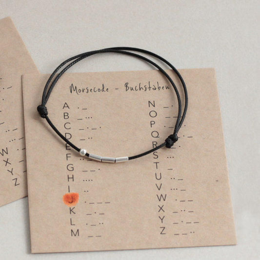 Morsecode Buchstaben auf ein Blatt gedruckt darauf liegend ein Armbändchen mit Morsecode Perlen.