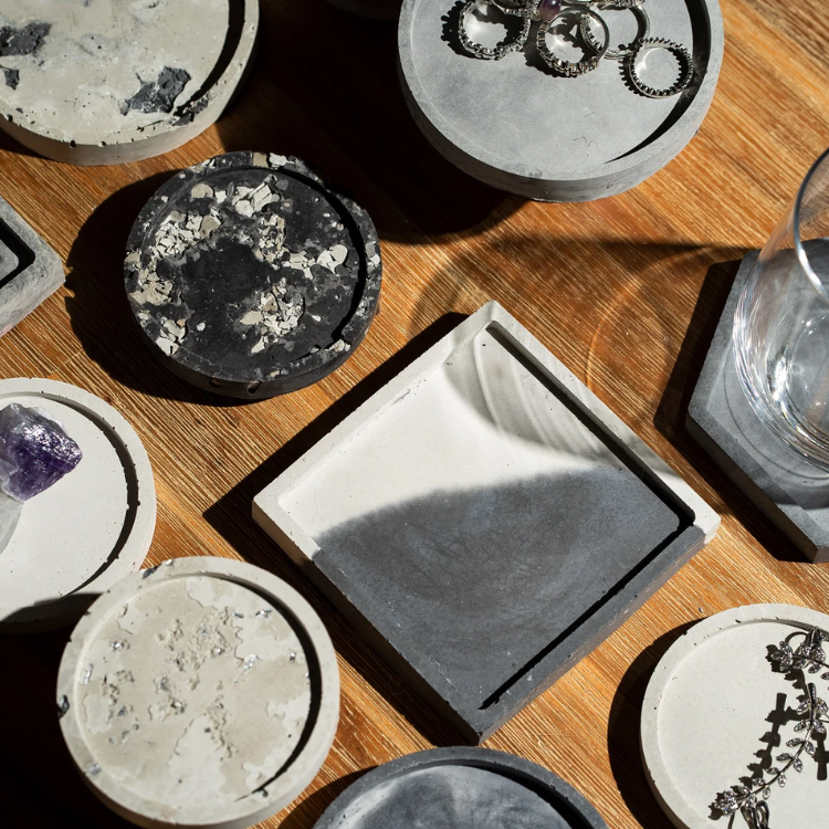 Flache Betonuntersetzer mit Mosaik und Einschlüssen stehen auf einem Tisch