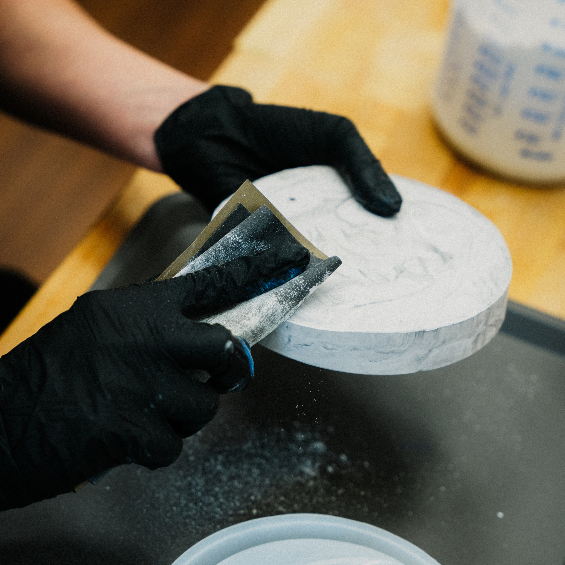 Eine Person mit schwarzen Handschuhen schleift ein Werkstück aus Beton glatt.