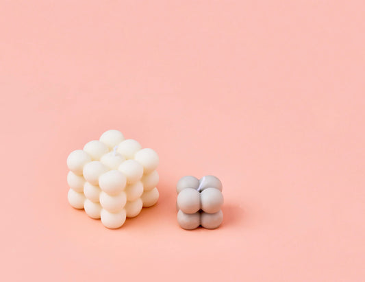 Zwei fertig gegossene Bubblekerzen eine kleine graue und eine doppelt so große weiße Bubblekerze auf rosa Hintergrund.