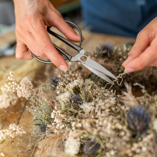Eine Person schneidet mit einer Schere einen Kranz aus Trockenblumen in einem Workshop für Kreative.