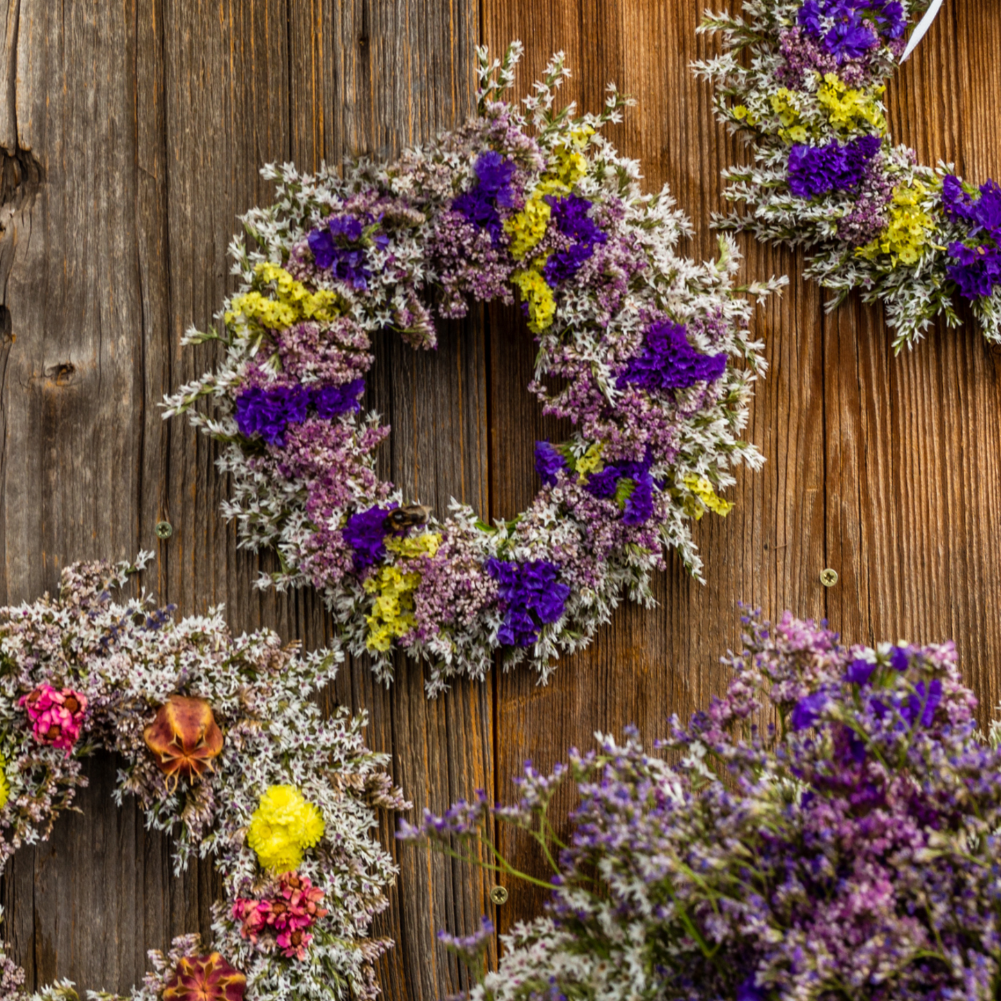 Vier bunte Trockenblumenkränze liegen auf einem Holztisch.