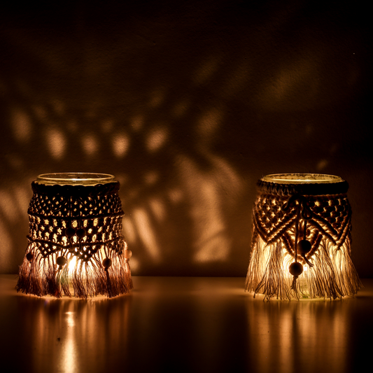 Zwei mit Makramee geknüpfte Windlichter stehen im Dunkeln mit Kerzen auf einem Tisch.