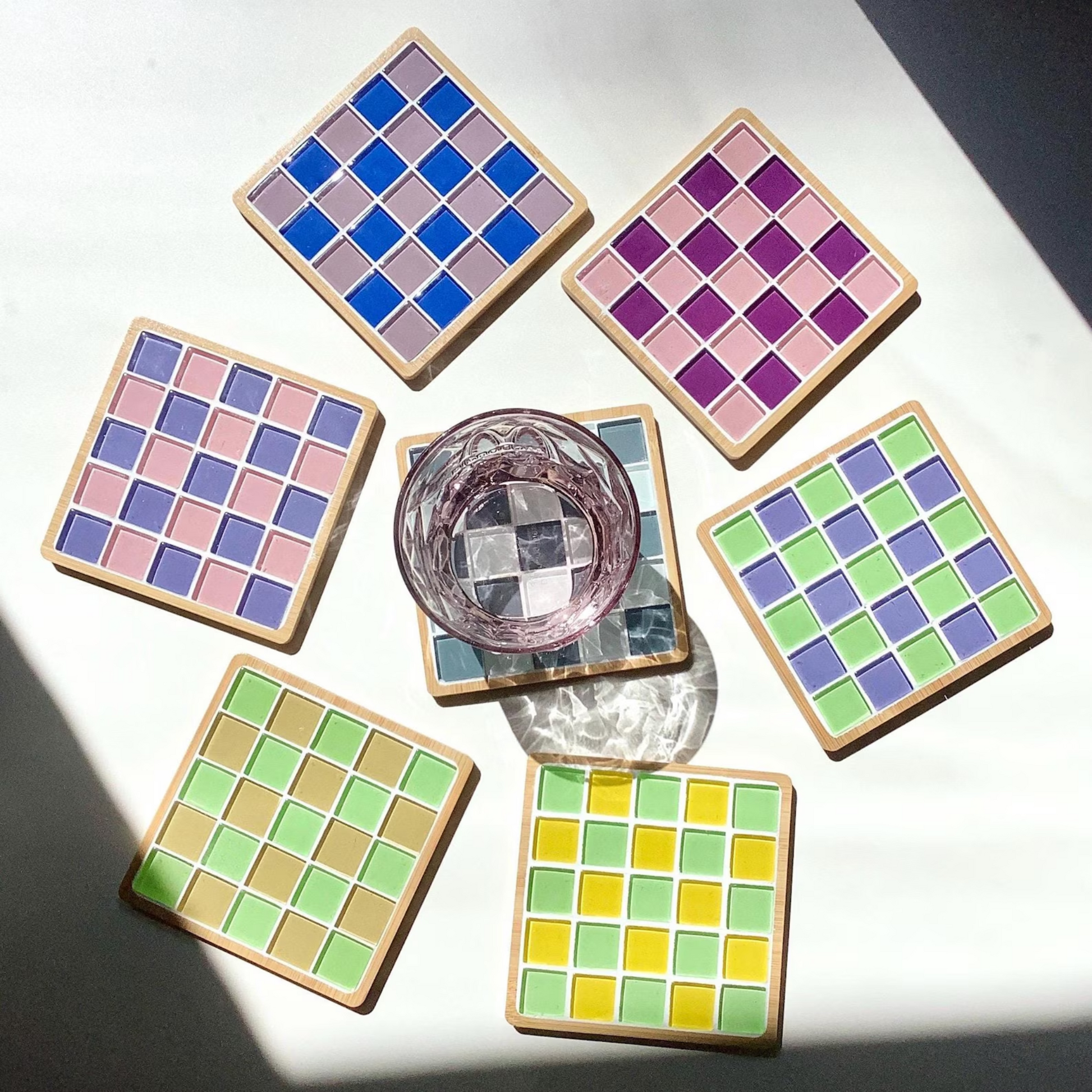 Sieben Mosaikuntersetzer in verschiedenen Farben als Struktur eines Schachbretts auf einem Tisch nebeneinander liegend.