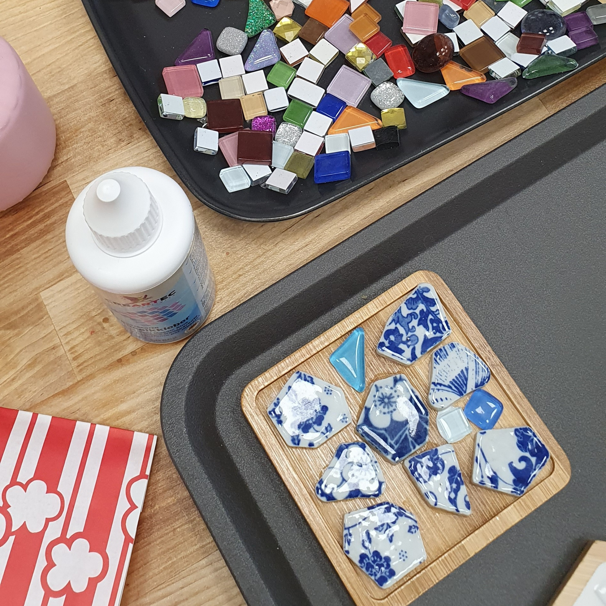 Utensilien für einen Mosaik Workshop stehen auf einem Tisch. Lose Mosaiksteine und ein Mosaikkleber.
