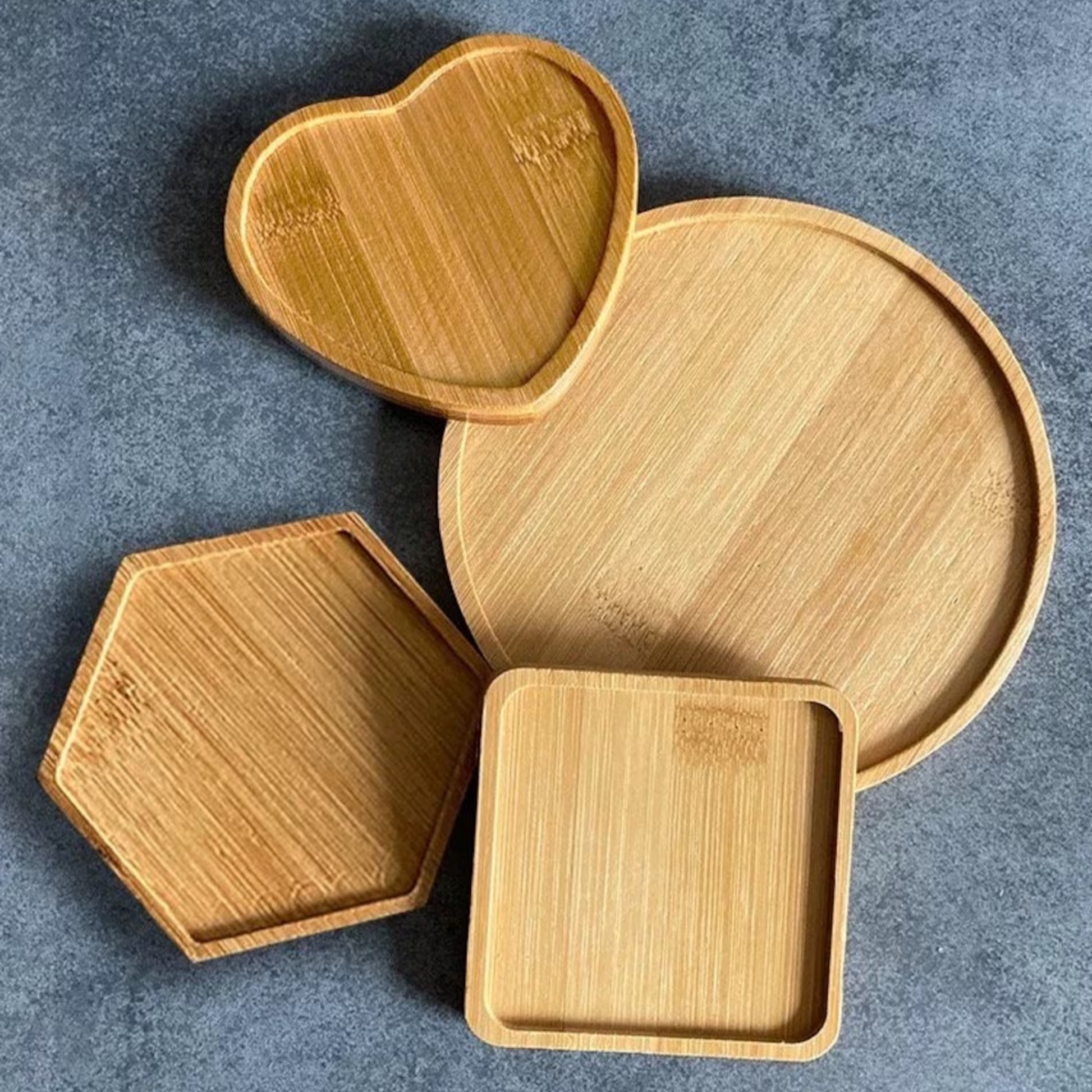 Vier Holzuntersetzer in hellem Holz oder Bambus in verschiedenen Formen liegen auf dem Tisch zur Vorbereitung eines Mosaik-Workshops.