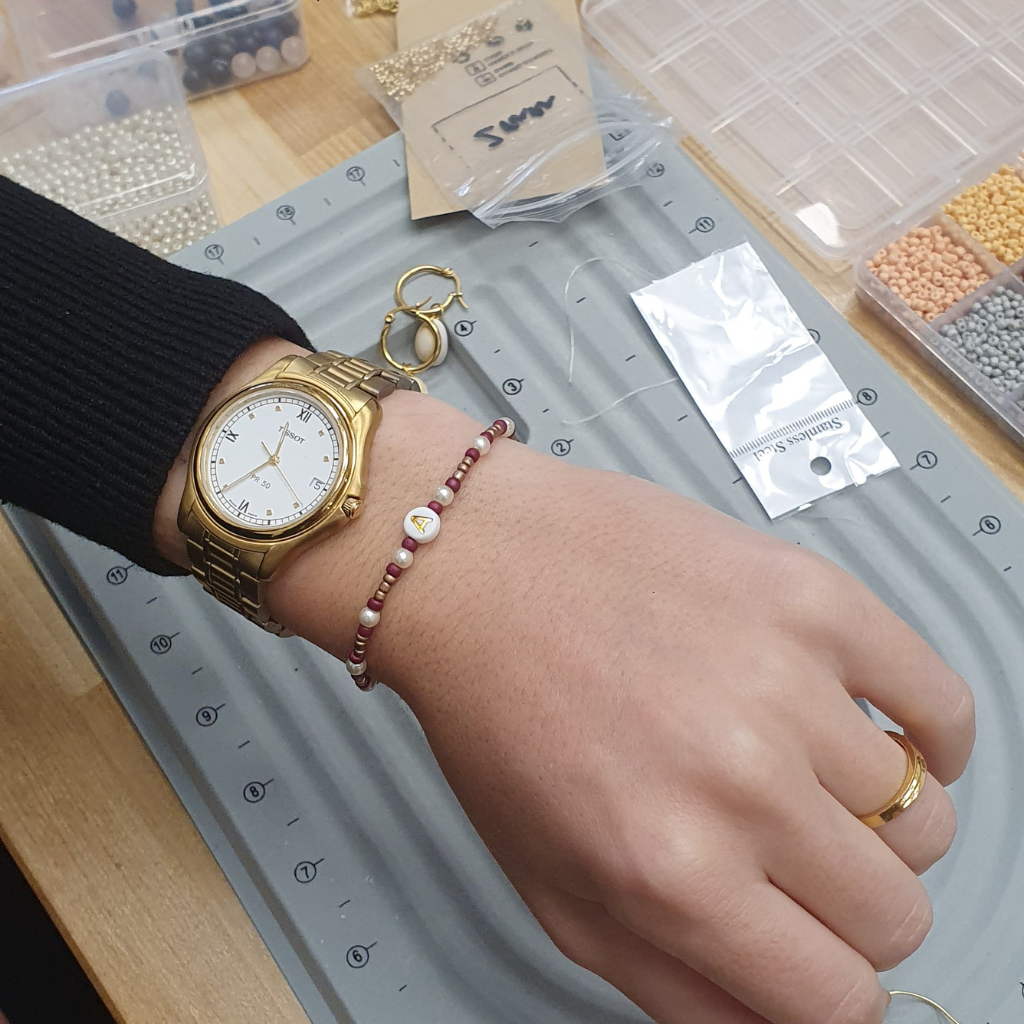 Hand einer Person mit einem fertigen Perlenarmband, das in einem Workshop im Kreativstudio München gefertigt wurde.