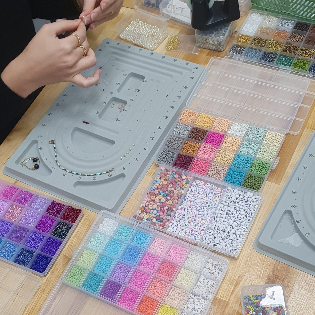 Tisch mit sehr vielen bunten Perlen in Sortierboxen zur Vorbereitung auf einen Workshop für Perlen und Prosecco.