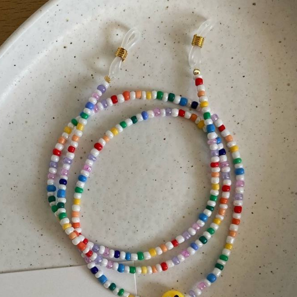 Eine fertige Perlenkette mit bunten Perlen liegt in einer Schale auf einem Tisch.