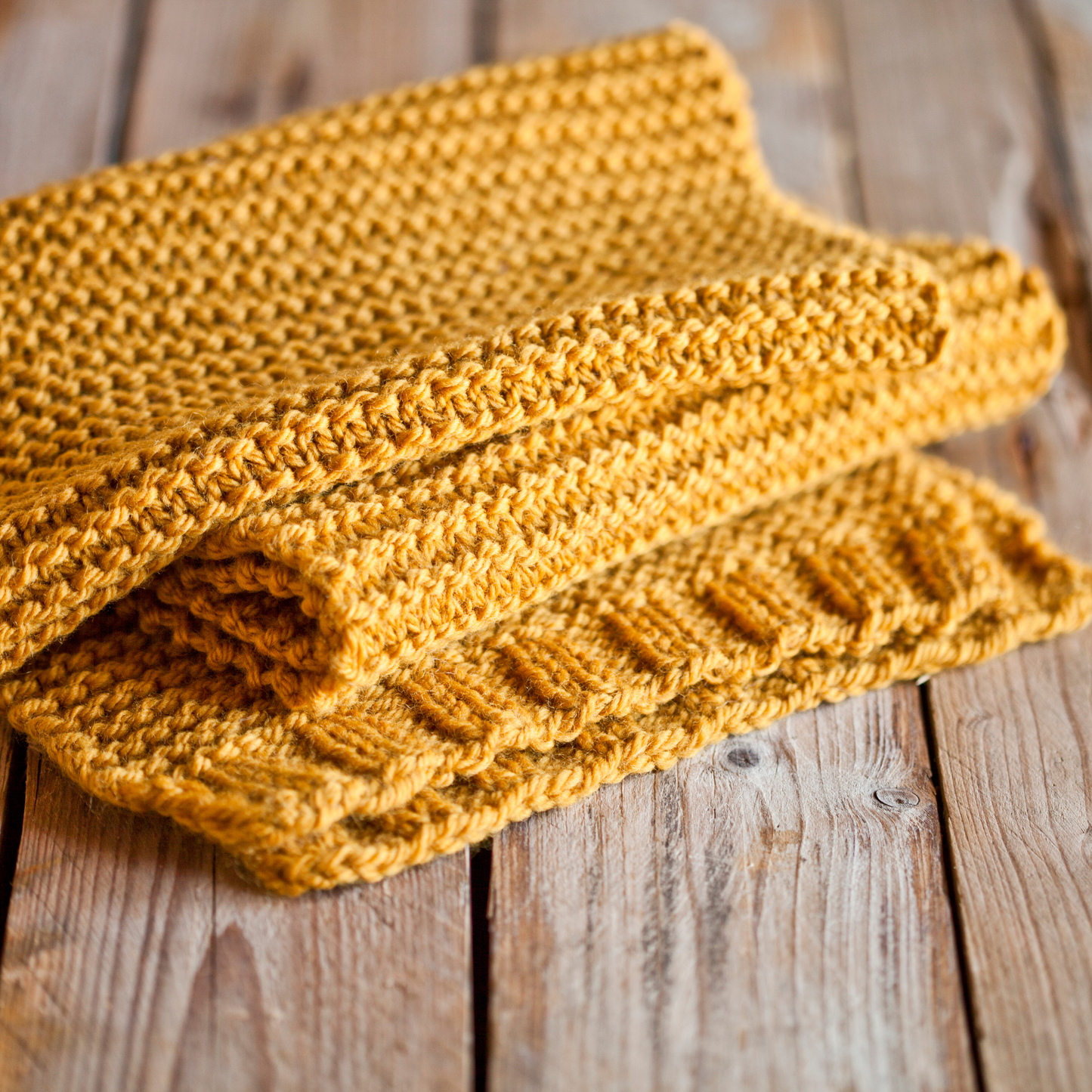 Ein oranger gestrickter Schal liegt auf einem Bretterboden.