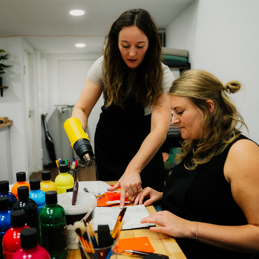 Zwei Frauen erstellen unter Anleitung der Einen ein Strukturbild mit Farben und Heißluftfön im Kreativstudio München im Arabellapark.