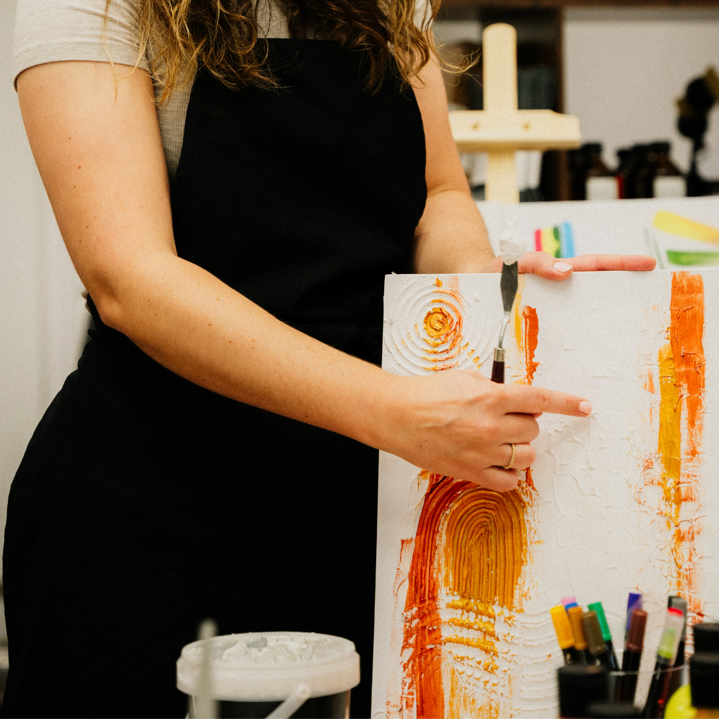 Kursleiterin mit schwarzer Schürze führt die Erstellung eines Strukturbildes im Kreativstudio München bei einem Workshop vor.