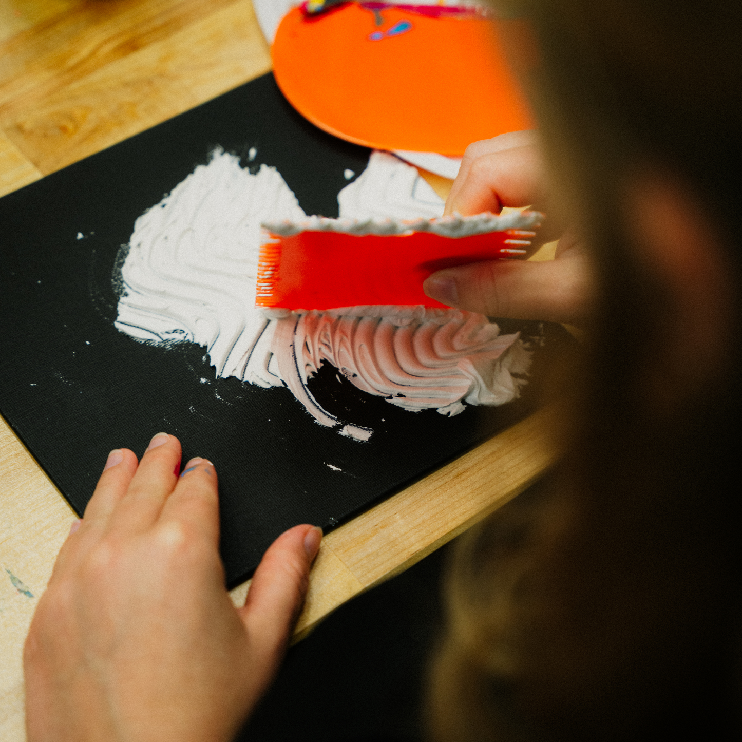 Person mit Spachtel erstellt ein Strukturbild auf schwarzem Tonpapier bei einem Strukturbilder-Workshop.