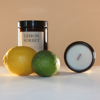 Kerze im Schraubglas stehend und eine Kerze liegend mit der Aufschrift Lemon Sorbet 120 g im Vordergrund eine Zitrone und Limette