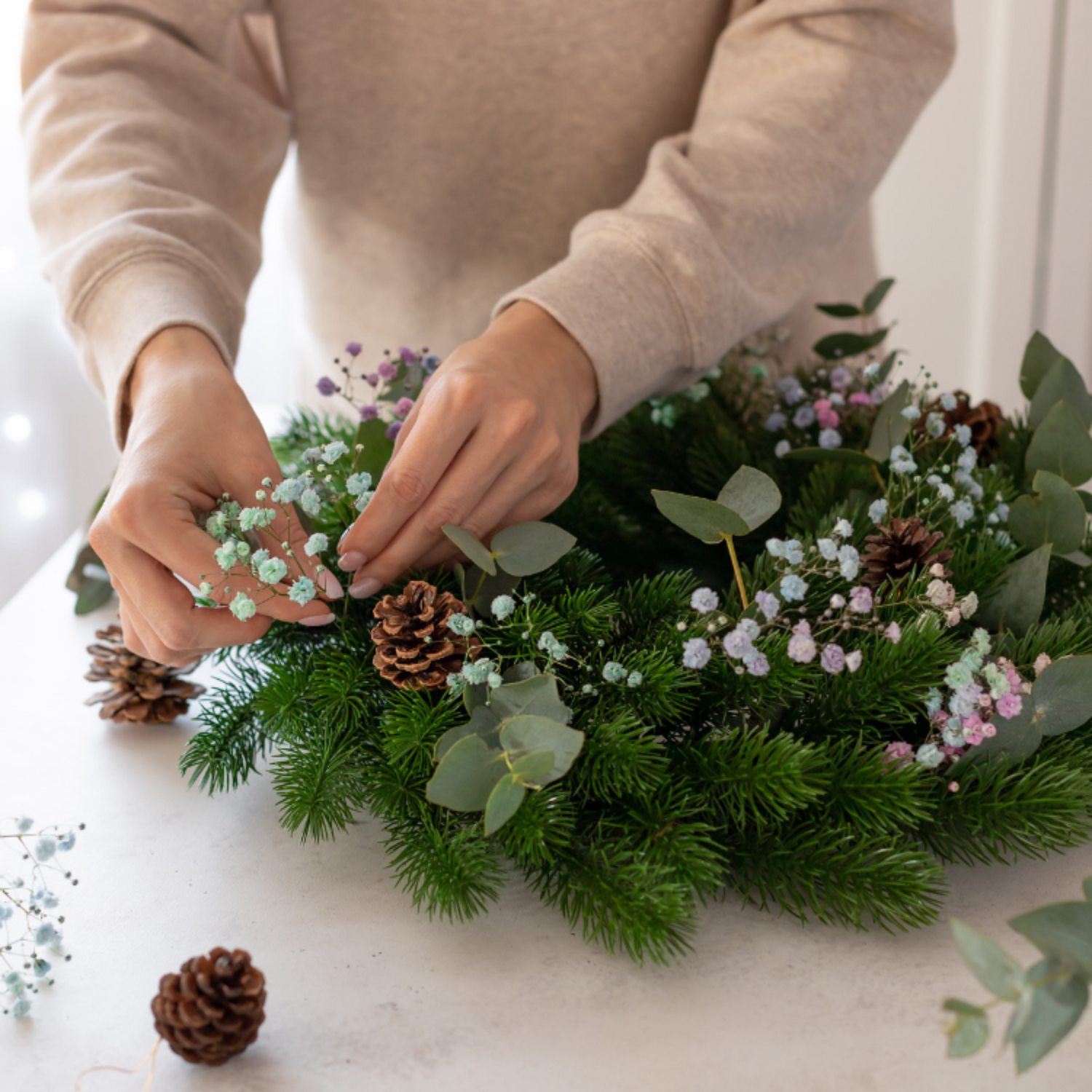Eine Person bindet mit Trockenblumen und Tannenzweigen einen Adventskranz in einem Workshop.