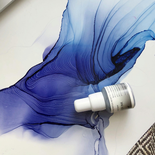 Weißes Blatt Papier mit kräftigen Blautönen mit der Technik Alkoholtinte gemalt. Außerdem ein Fläschchen Alkoholtinte liegend auf dem Bild.
