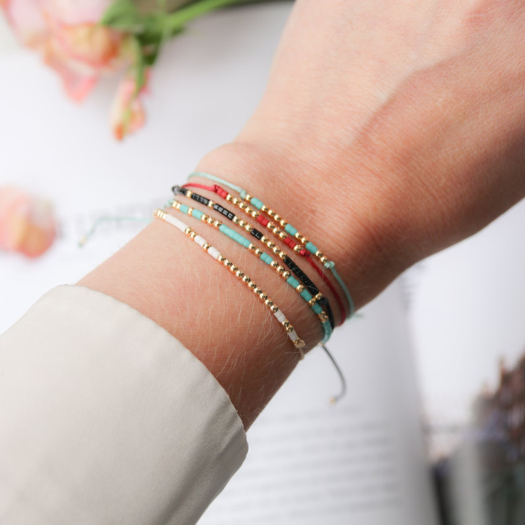 Handgelenk mit fünf verschieden geknüpften Armbändern im Hintergrund eine Blume und ein Schriftstück.