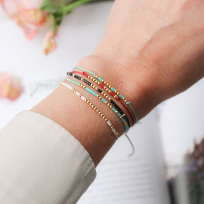Handgelenk mit fünf verschieden geknüpften Armbändern im Hintergrund eine Blume und ein Schriftstück.