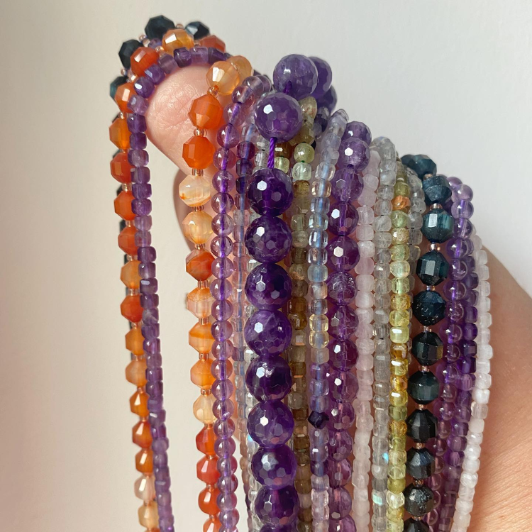 Auf einem Daumen hängend aufgereihte Armbänder aus verschiedenen Kristallen oder Perlen.