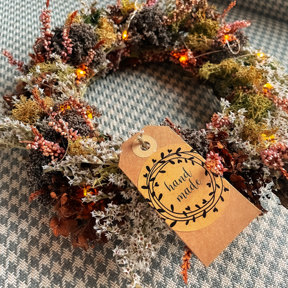 Ein Kranz aus Trockenblumen und frischen Blumen liegend auf einem Tisch mit einem Anhänger mit der Aufschrift handmade.