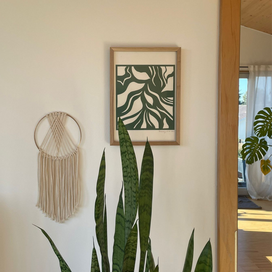 Hängendes mit der Technik Papercut erstelltes Bild hängend an der Wand in einer Wohnung, daneben Pflanzen und ein Traumfänger