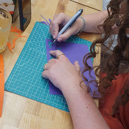 Eine lockige Frau ist gerade in einem papercut Workshop und erstellt ein Kunstwerk an einem Arbeitstisch.