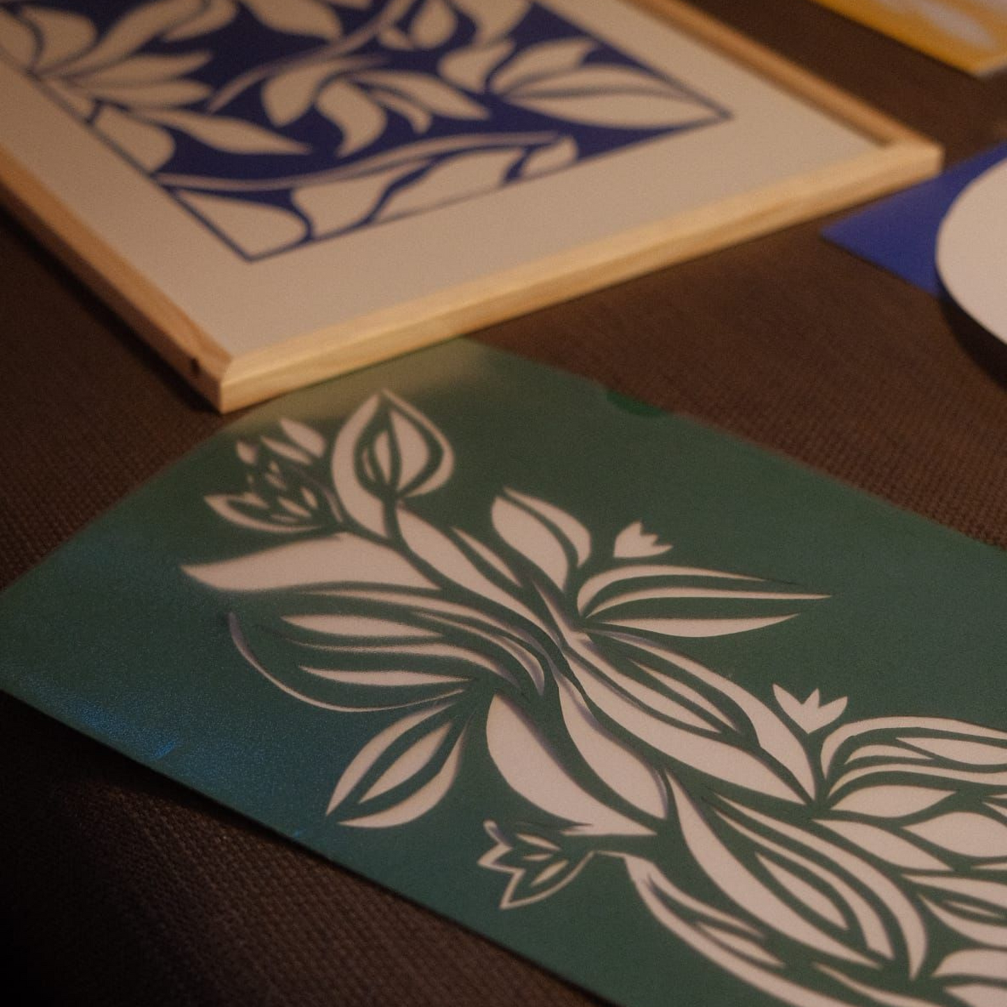 Zwei Kunstwerke liegend auf einem Tisch mit der Technik papercut in einem Workshop erstellt in den Farben grün und blau.