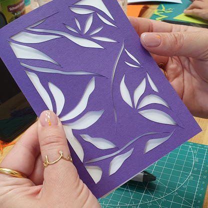 Hände halten ein halbfertiges Kunstwerk in der Größe A5 in der Farbe lila mit verschiedenen Mustern der Technik paperut.
