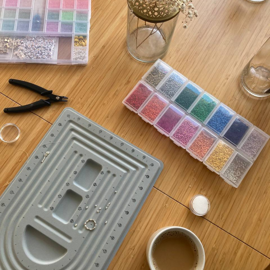 Eine Sortierbox mit bunten kleinen Perlen und einer Messschablone liegen auf einem Tisch, daneben das Werkzeug für einen Workshop.
