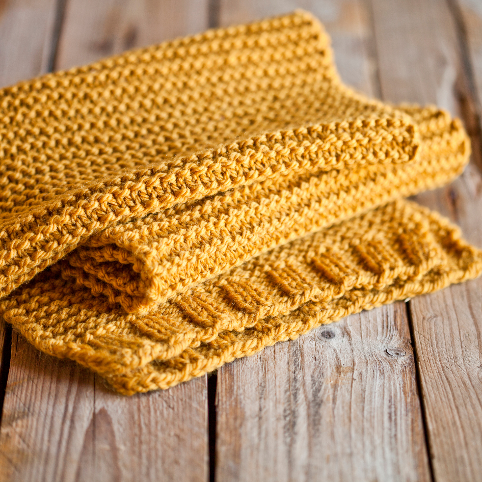 Ein oranger gestrickter Schal liegt auf einem Bretterboden.
