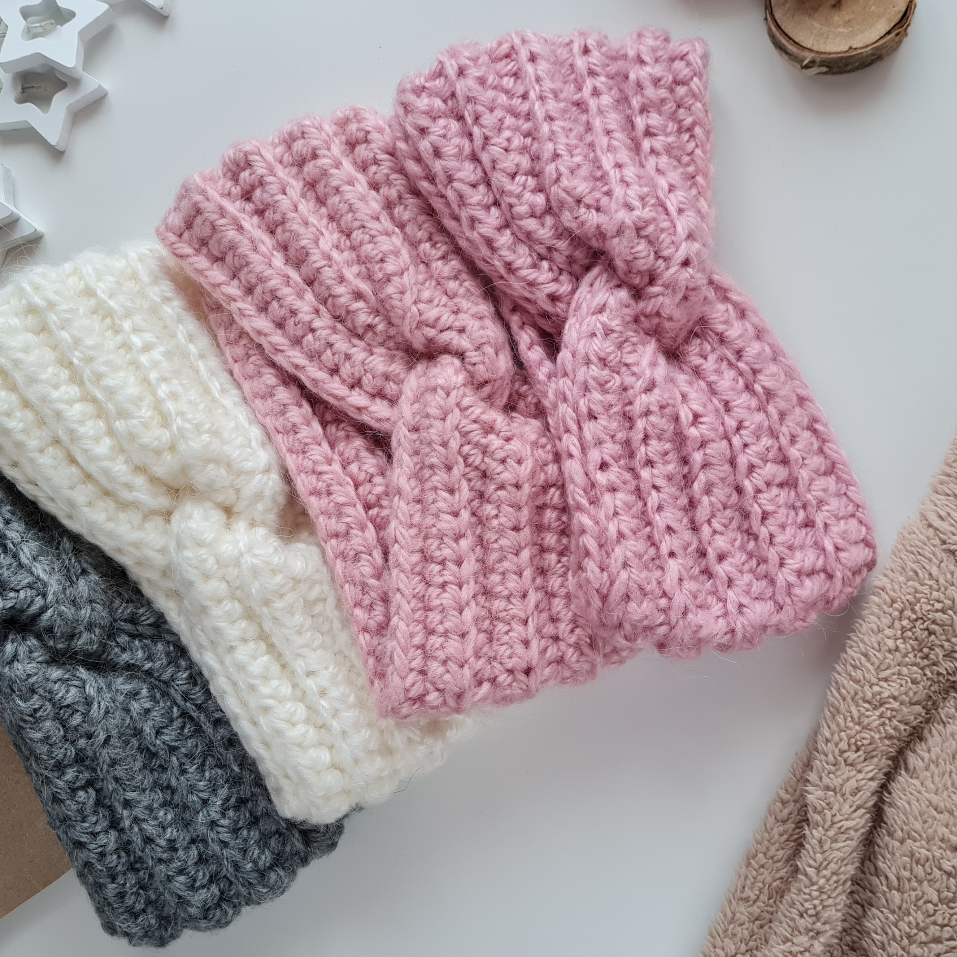 Gestrickte Stirnbänder in verschiedenen Farben liegen auf einem weißen Tisch mit Sternen im Hintergrund.