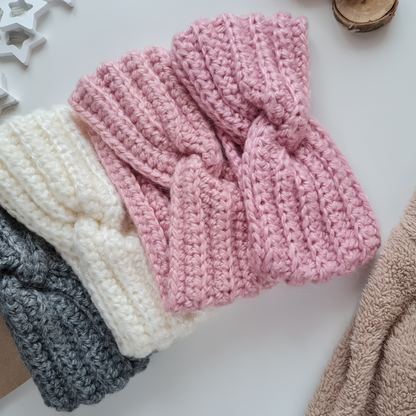 Gestrickte Stirnbänder in verschiedenen Farben liegen auf einem weißen Tisch mit Sternen im Hintergrund.