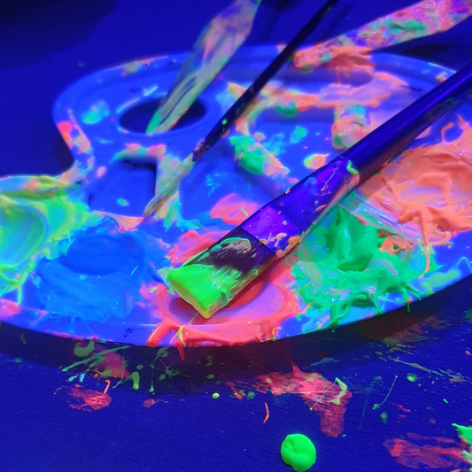 Pinsel und eine Malerfarbpalette sind mit Neonfarben bemalt und leuchten im UV-Licht beim Techno & Paint Workshop Schwarzlicht Edition.